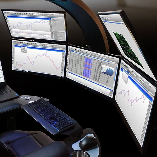 Dark office chair in front of a desk with multiple computer monitors displaying financial charts.